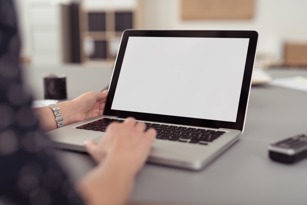 Businesswoman sitting at her desk navigating the internet on a laptop computer using the trackpad, over the shoulder view of the blank screen.jpeg